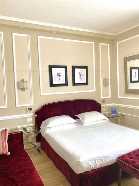 Calzaluoli Hotel Suite with burgundy velvet headboard, fainting couch, and foot rest.